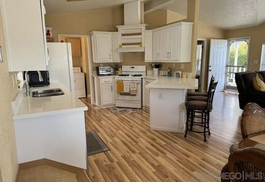 12250 Vista Del Cajon Road, Unit 25 El Cajon, CA 92021 - Photo 10 of 39 a kitchen with stainless steel appliances a stove top oven a refrigerator a dining table and chairs with wooden floor