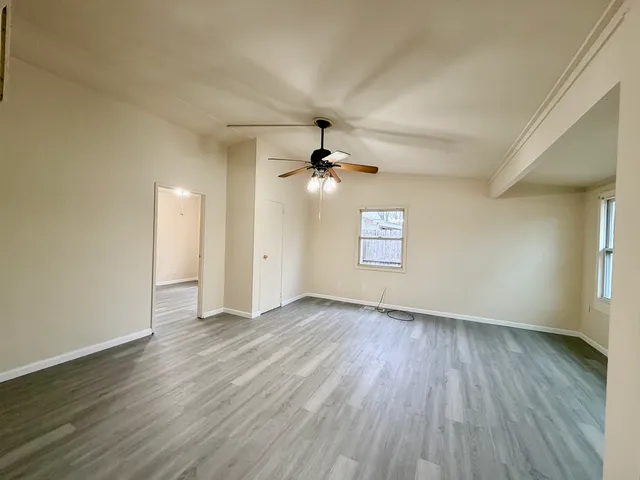 an empty room with wooden floor ceiling fan and window