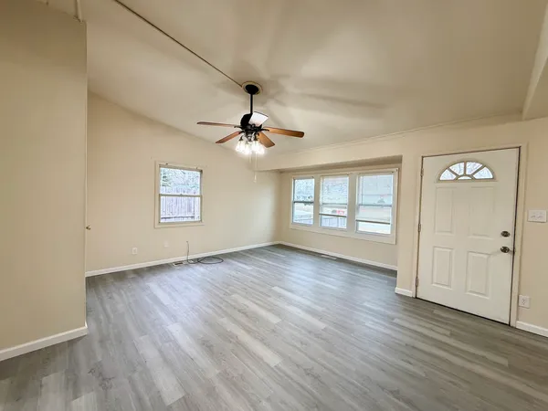 an empty room with wooden floor chandelier fan and windows