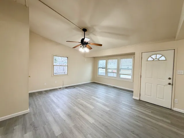 an empty room with wooden floor chandelier fan and windows