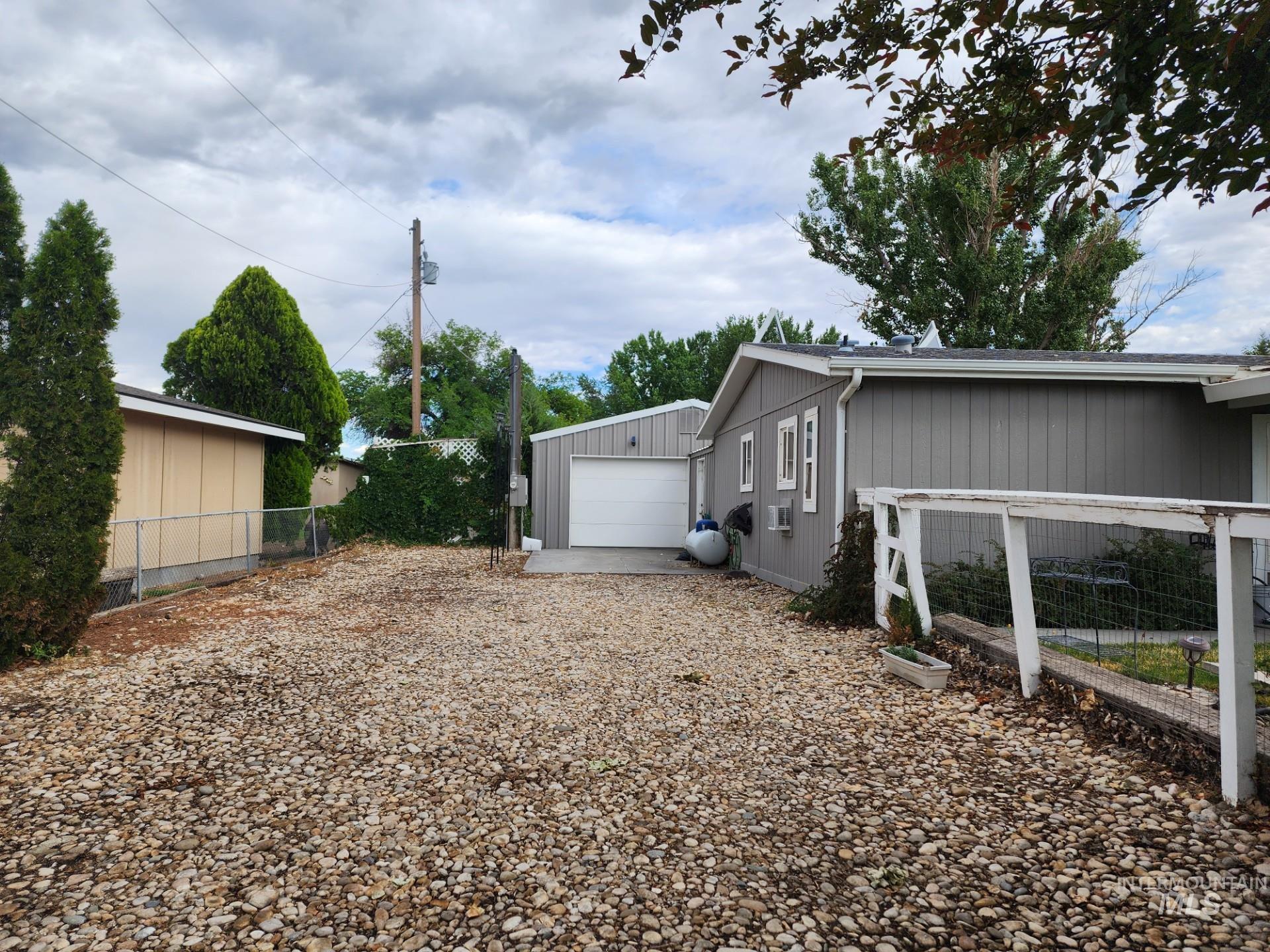 235 5th Street Grand View, ID 83624 - Photo 3 of 22 Expansive gravel parking area with chain-link fencing, mature perimeter trees, and a detached garage featuring a white overhead door