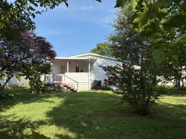 a white house with a big yard plants and large trees