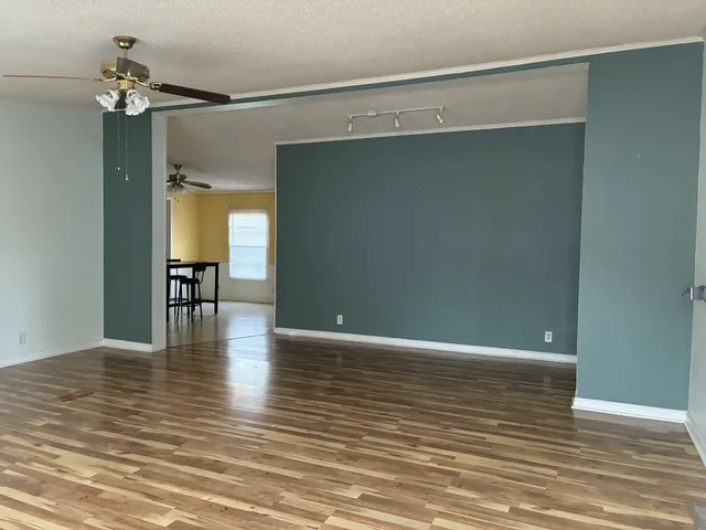 a view of an empty room with wooden floor and a ceiling fan