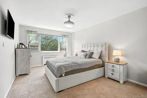 a spacious bedroom with a bed and a flat tv screen on dresser