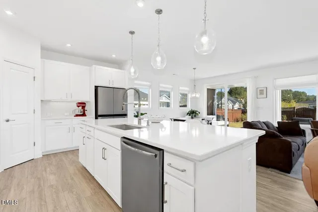 a large white kitchen with a large island oven a sink and dishwasher with wooden floor
