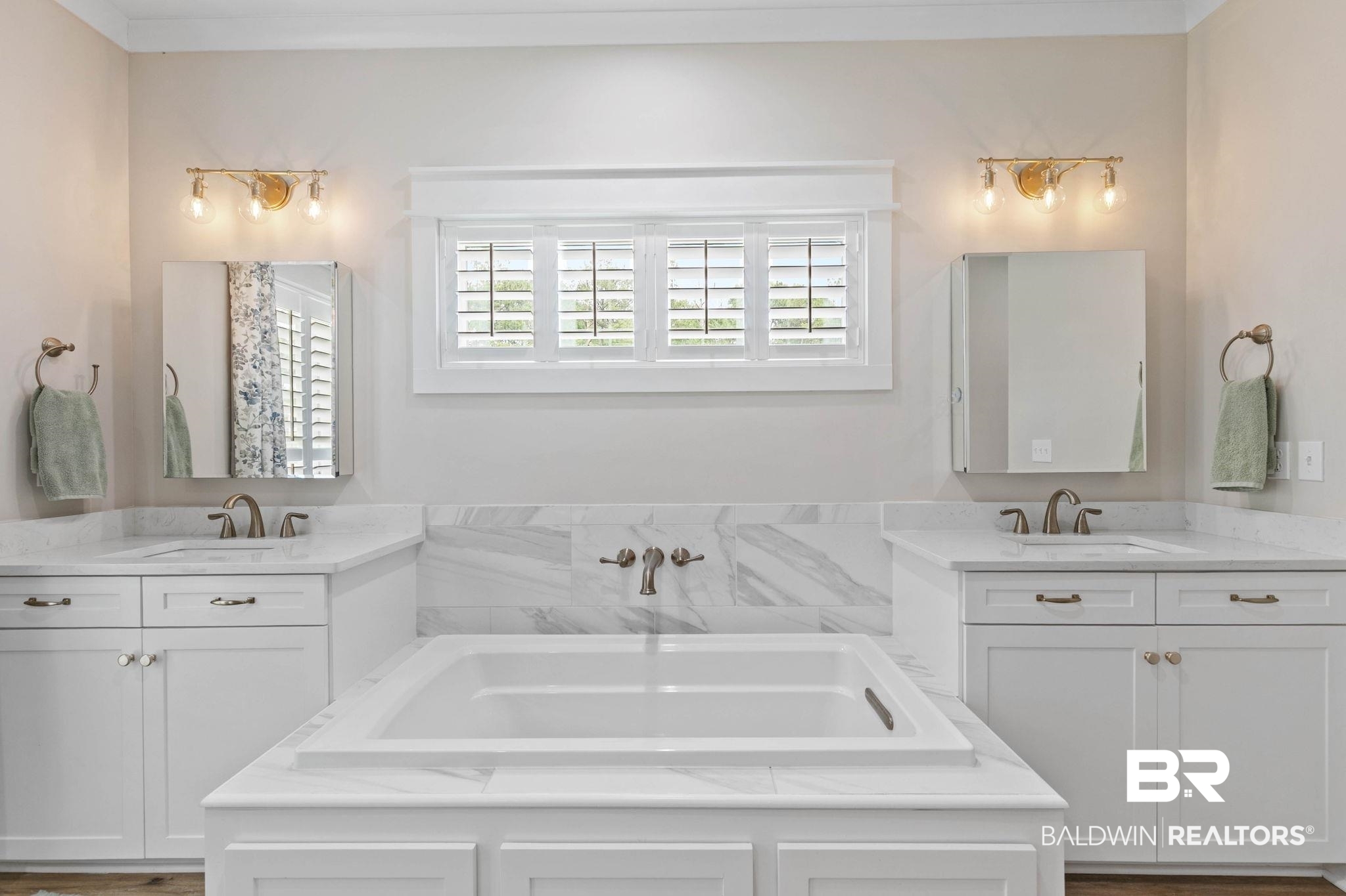 2029 George Lee Road Repton, AL 36475 - Photo 28 of 58 Bathroom featuring a built-in tub with a marble surround, two single vanities with marble countertops and undermount sinks, white shaker cabinetry, and wall-mounted gold-finish light fixtures