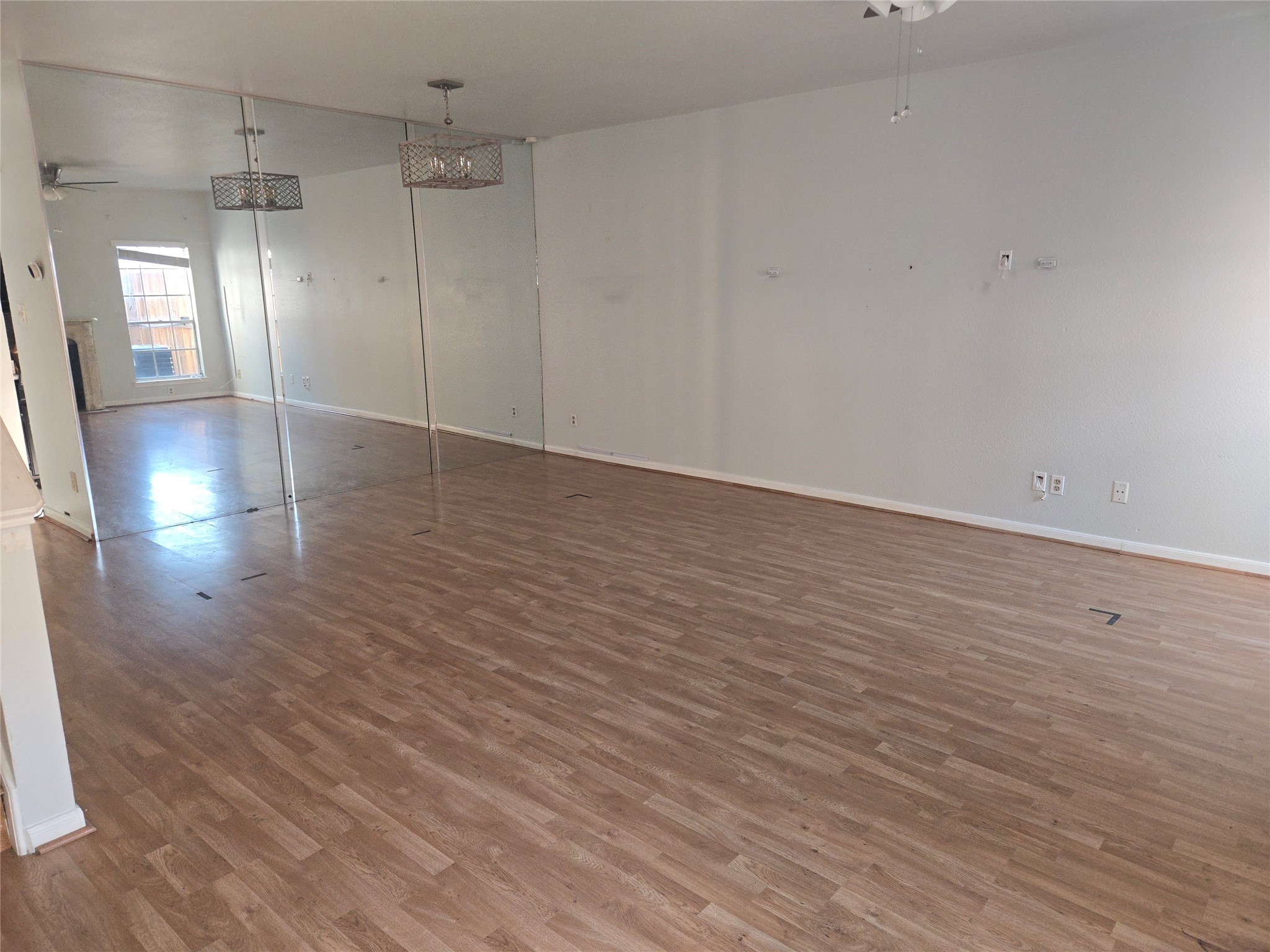 3780 Tanglewilde Street, Unit 501 Houston, TX 77063 - Photo 16 of 26 Spacious, open-concept room with light wood like flooring and mirrored wall, enhancing natural light. Modern pendant lighting and large window offer a bright, versatile living area.
