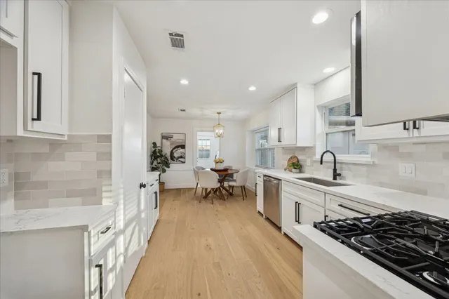 a large white kitchen with lots of counter top space a sink stainless steel appliances and cabinets