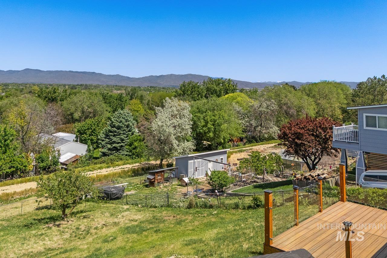 10178 West Fox Ridge Drive Boise, ID 83709 - Photo 27 of 36 Expansive outdoor living area featuring a wooden deck with glass panel railing, a sloping lawn, and distant mountains