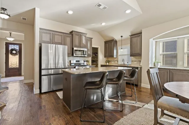 a kitchen with stainless steel appliances granite countertop a refrigerator a stove a sink a dining table and chairs with wooden floor