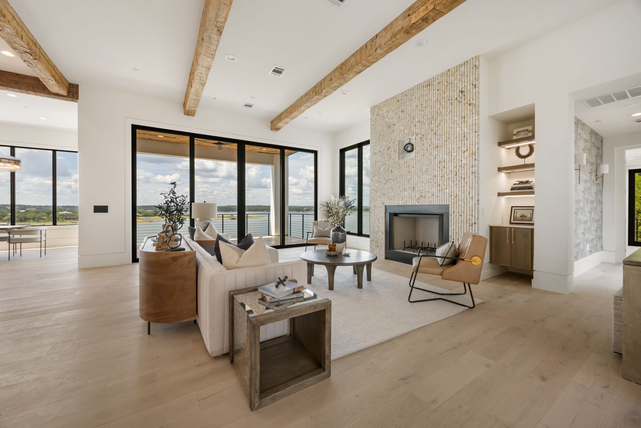 1496 Buffalo Gap Road Lakeway, TX 78734 - Photo 10 of 37 Exposed wood beams crown this elegant living area, featuring a cozy fireplace and expansive glass doors opening to captivating water views.