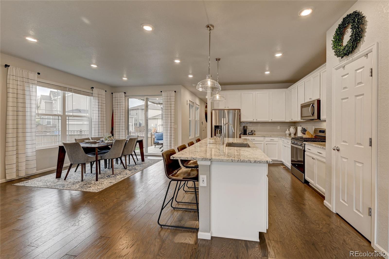 7203 Bedlam Drive Castle Pines, CO 80108 - Photo 12 of 39 a kitchen with stainless steel appliances granite countertop a stove top oven a refrigerator a dining table and chairs with wooden floor