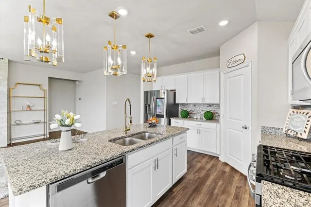 a kitchen with stainless steel appliances a sink a stove a microwave a refrigerator a center island and cabinets