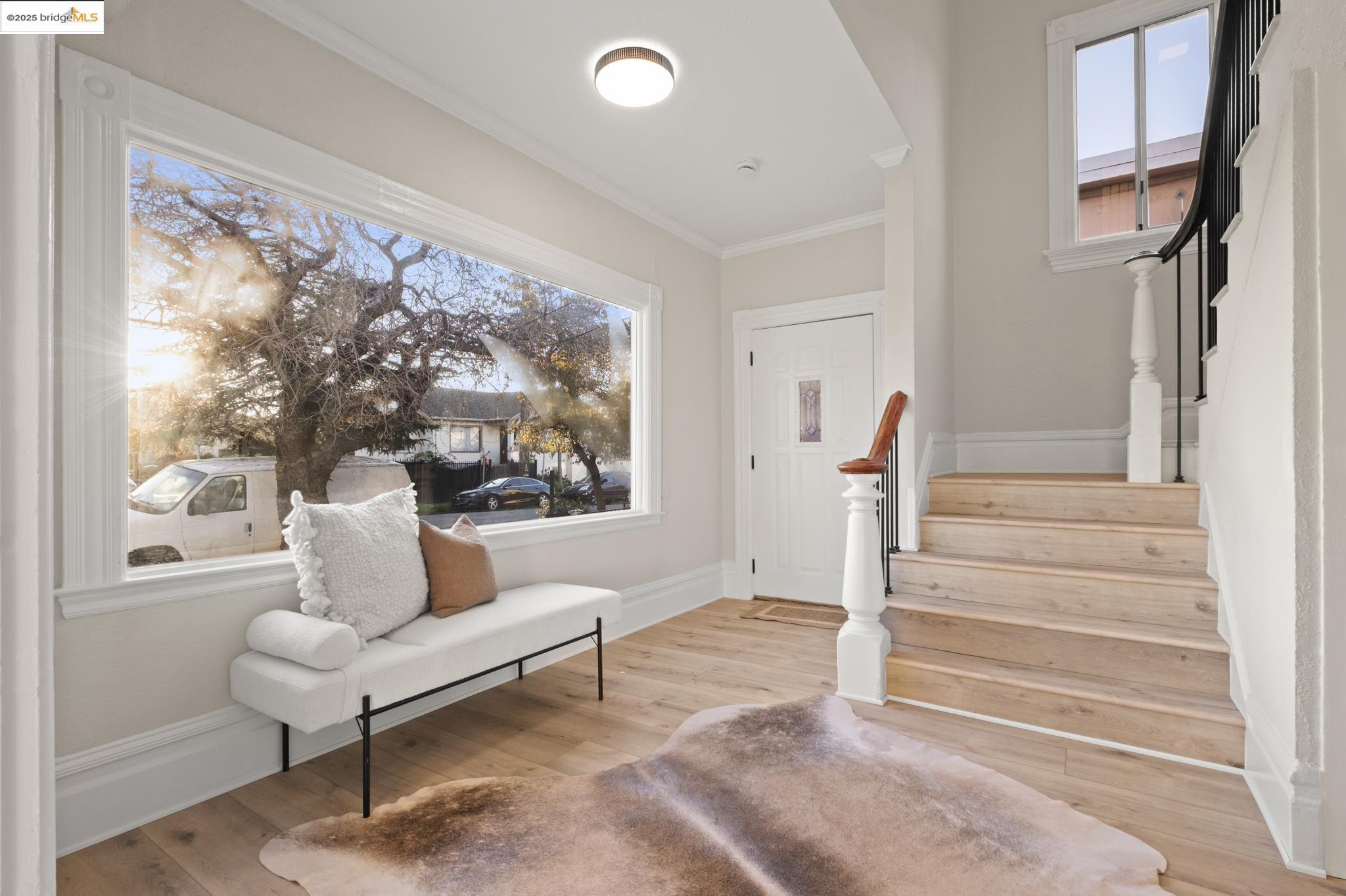 Foyer entrance with stairs, healthy amount of natural light, light wood-type flooring, and crown molding