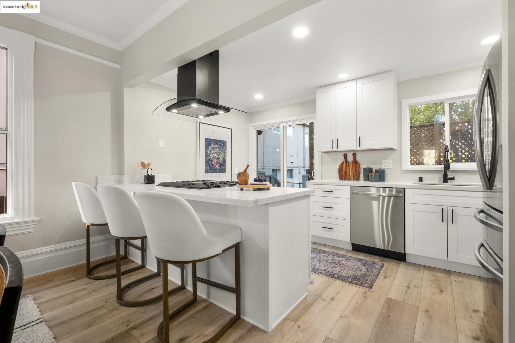 2050 East 30th Street Oakland, CA 94606 - Photo 13 of 48 Kitchen with ornamental molding, a breakfast bar, white cabinets, appliances with stainless steel finishes, and light wood finished floors