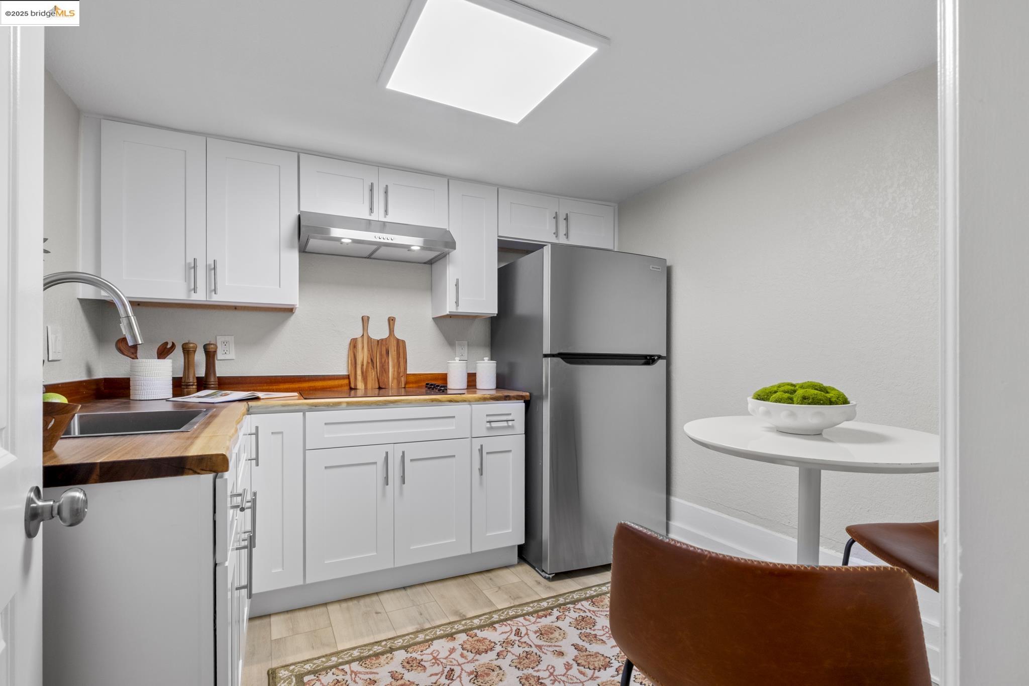 2050 East 30th Street Oakland, CA 94606 - Photo 33 of 48 Kitchen with butcher block counters, white cabinets, freestanding refrigerator, light wood-style flooring, and under cabinet range hood