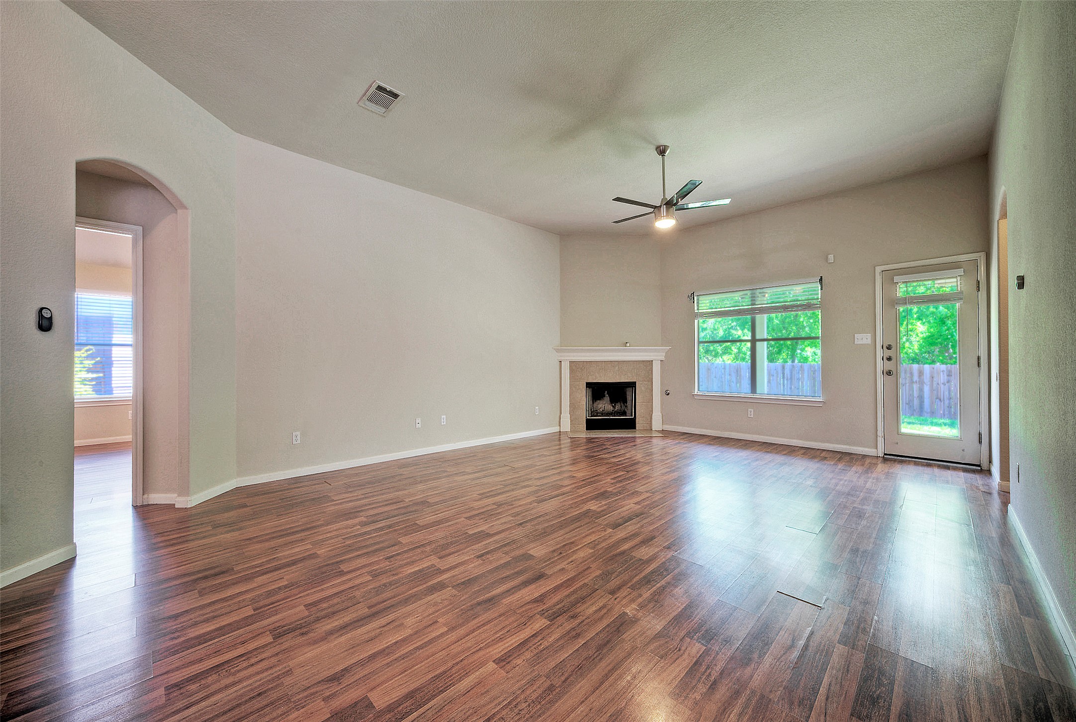 400 Pheasant Ridge Drive Round Rock, TX 78665 - Photo 16 of 29 Spacious living area featuring wood-finish flooring, a vaulted ceiling with a ceiling fan, a fireplace with a light-colored mantel, large windows, and a glass-paneled exterior door