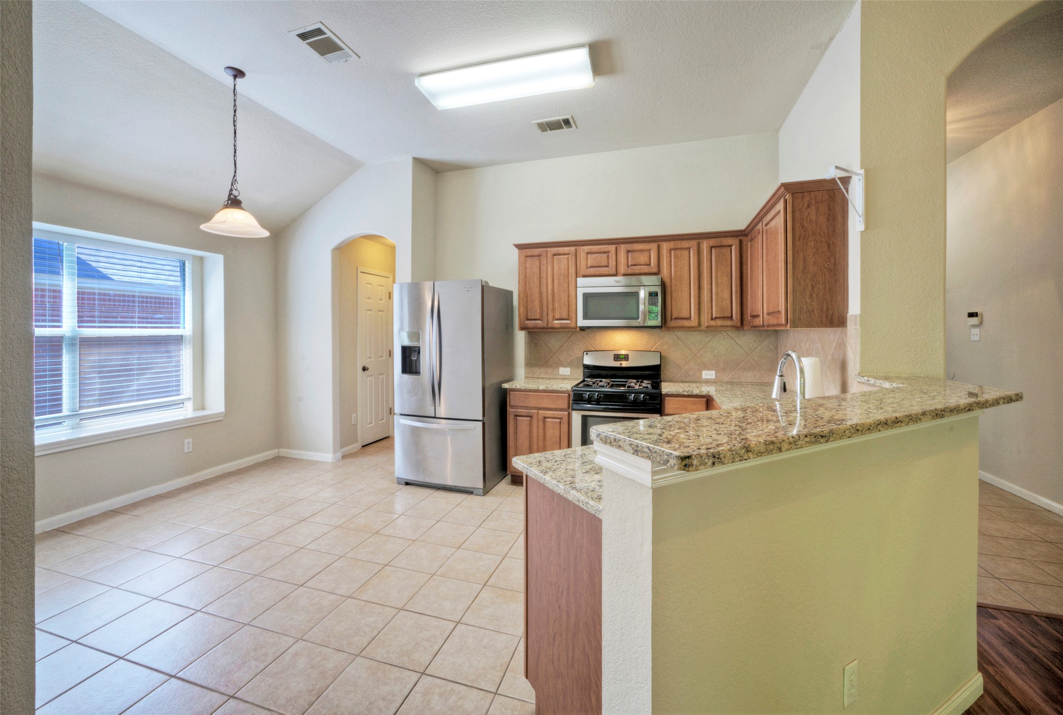 400 Pheasant Ridge Drive Round Rock, TX 78665 - Photo 17 of 29 Kitchen and dining area featuring tile flooring, wooden cabinetry, stainless steel appliances, a breakfast bar with stone countertops, and an arched doorway