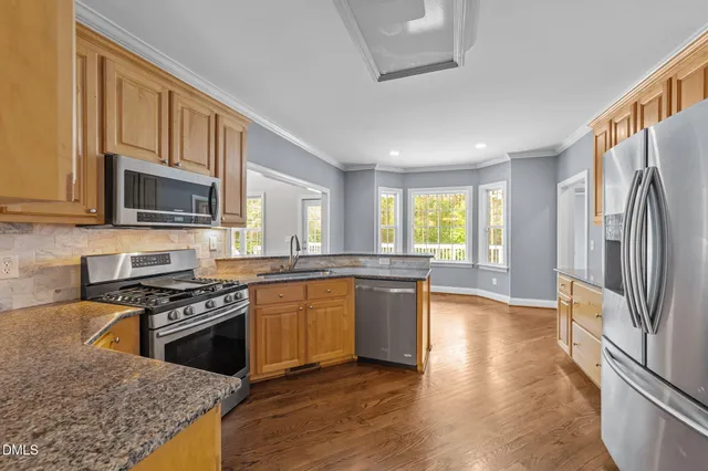 a kitchen with stainless steel appliances granite countertop a stove a sink dishwasher a refrigerator white cabinets granite counter tops and a window