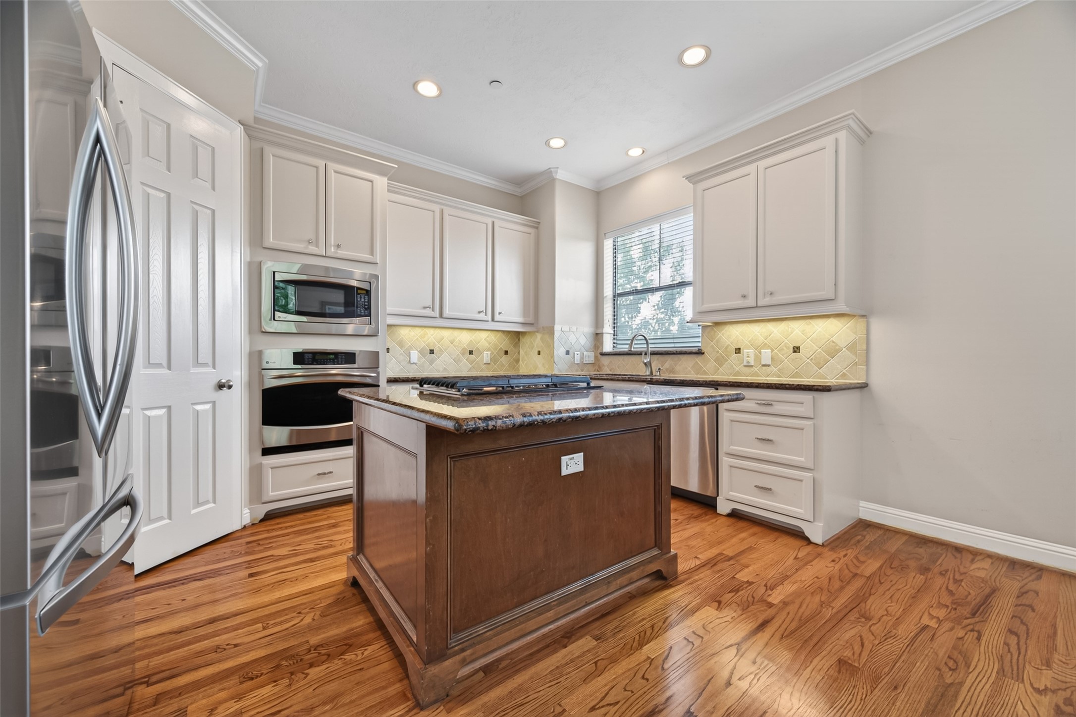 2611 Riverside Drive, Unit C Houston, TX 77004 - Photo 18 of 50 This kitchen features hardwood floors, white cabinetry, and granite countertops. It includes stainless steel appliances, an island with a cooktop, and recessed lighting, offering a bright and modern space.