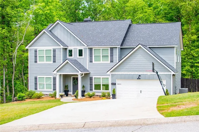a white house with a yard plants and large tree