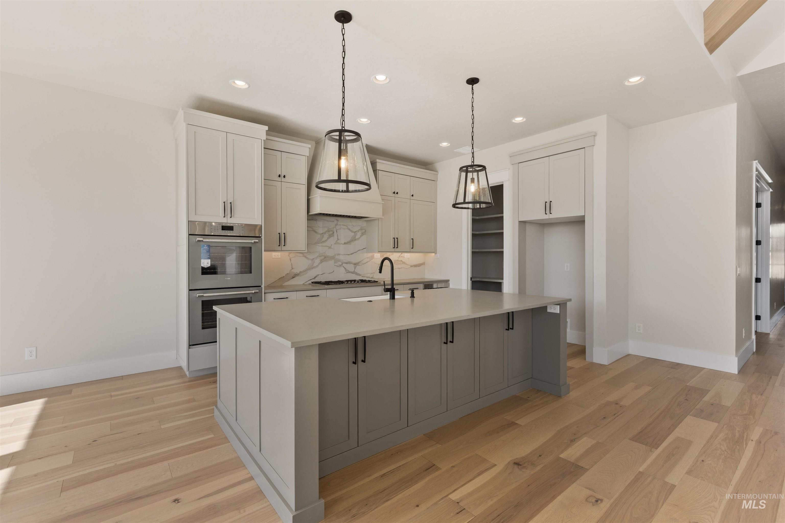 5857 South Highmark Avenue Meridian, ID 83642 - Photo 9 of 37 Kitchen featuring decorative backsplash, double oven, recessed lighting, an island with sink, and light countertops