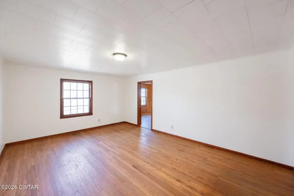 a view of an empty room with wooden floor and window