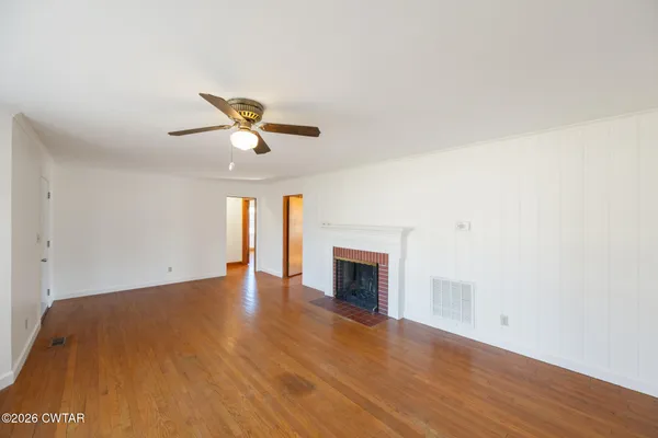 a view of an empty room with wooden floor and a fireplace