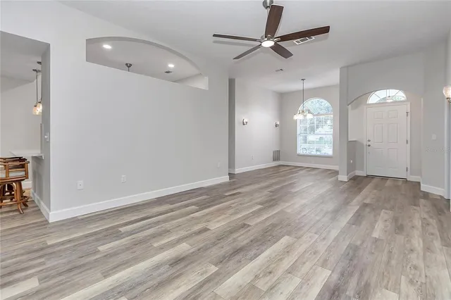 an empty room with wooden floor chandelier fan and windows
