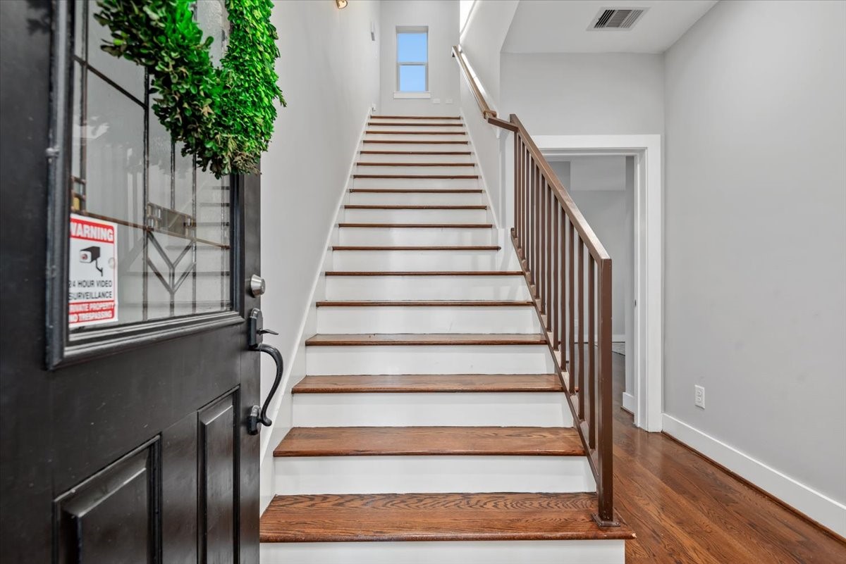 1005 Bingham Street, Unit 5 Houston, TX 77007 - Photo 22 of 50 This photo shows a welcoming entrance with a wooden staircase leading upward. The staircase features a modern railing, and the area is well-lit, showcasing hardwood floors and neutral walls for a clean, contemporary look.