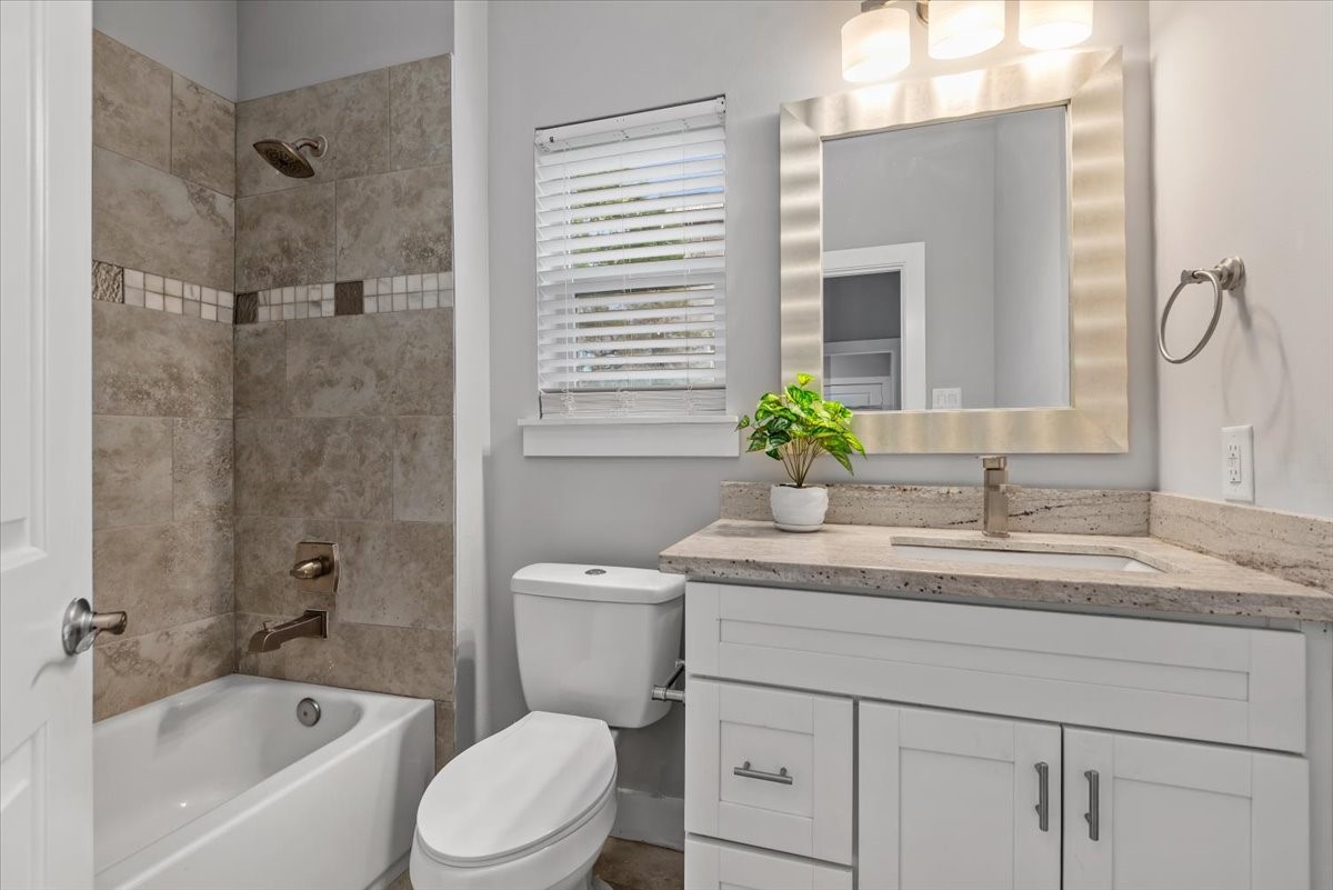 1005 Bingham Street, Unit 5 Houston, TX 77007 - Photo 24 of 50 This bathroom features a modern design with a white vanity, framed mirror, and stone countertop. It includes a shower-tub combo with elegant tilework, complemented by a large window for natural light.