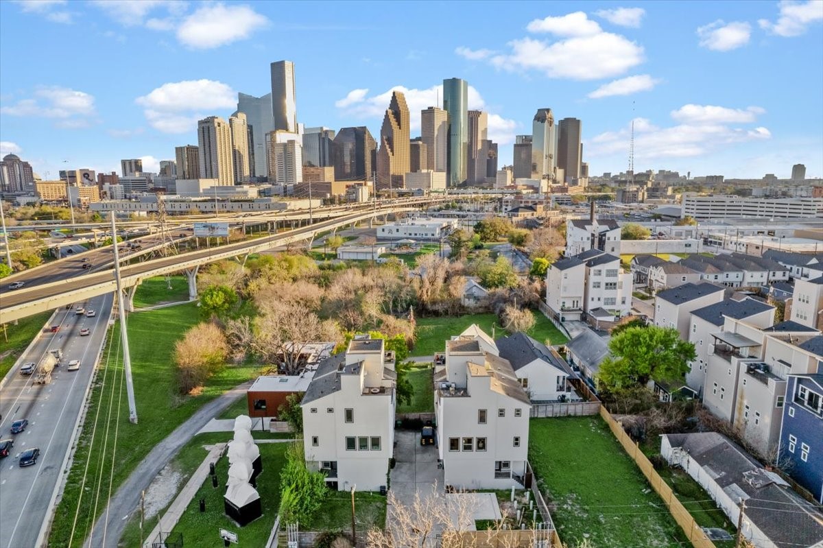 1005 Bingham Street, Unit 5 Houston, TX 77007 - Photo 28 of 50 This photo showcases a residential neighborhood with modern homes, located near a freeway. The area features green spaces and is set against a backdrop of a vibrant city skyline, suggesting a convenient urban lifestyle with easy access to city amenities.