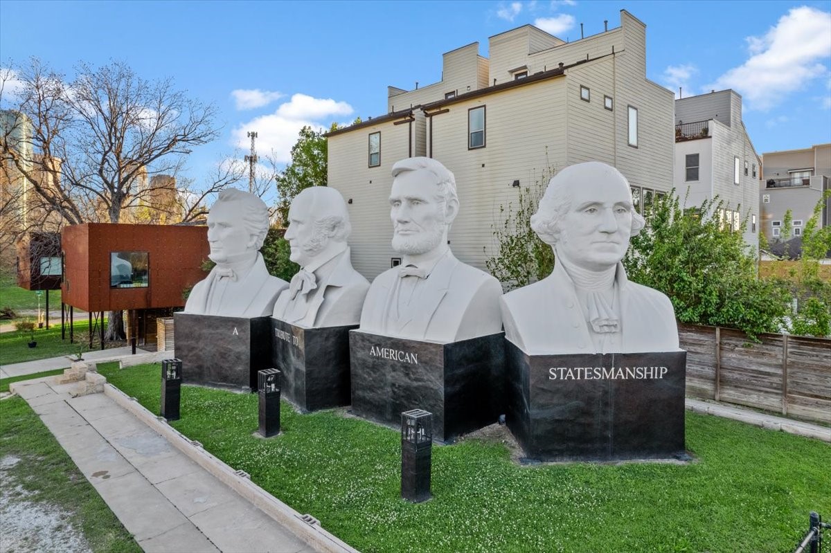 1005 Bingham Street, Unit 5 Houston, TX 77007 - Photo 29 of 50 This photo shows a unique outdoor area featuring the American Statesmanship Park featuring large busts of historical figures against a backdrop of modern small, gated community where the home is located. The picture also displays the unique industrial style "tree house" on the left side. The setting combines historical and contemporary elements, offering a distinctive neighborhood vibe.
