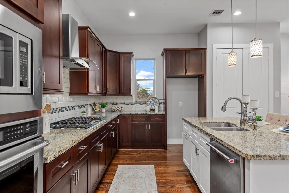 1005 Bingham Street, Unit 5 Houston, TX 77007 - Photo 31 of 50 This kitchen features elegant dark wood cabinets, granite countertops, and stainless steel appliances. It includes a central island with a sink and modern pendant lighting, offering a stylish and functional cooking space.