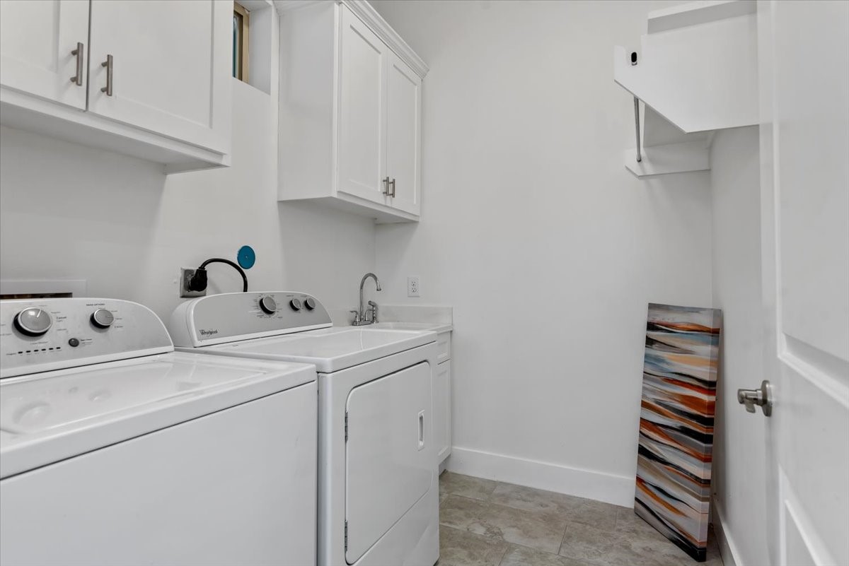 1005 Bingham Street, Unit 5 Houston, TX 77007 - Photo 33 of 50 This photo shows a clean, well-organized laundry room featuring a washer and dryer, upper cabinets for storage, a sink, and neutral-colored walls and flooring.
