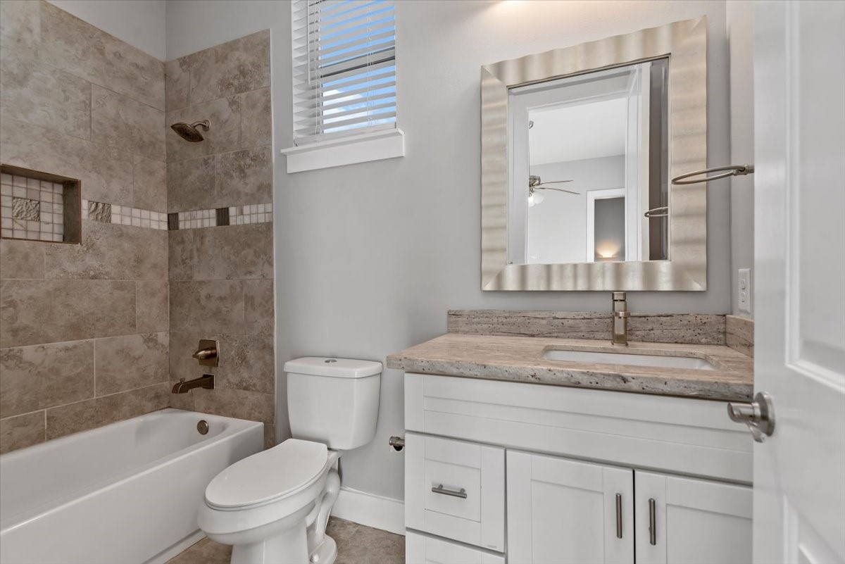 1005 Bingham Street, Unit 5 Houston, TX 77007 - Photo 35 of 50 This bathroom features a modern design with neutral tones. It includes a tiled shower-tub combo, a sleek vanity with a granite countertop, and a large mirror. Natural light filters in through a window with blinds, creating a bright and inviting space.