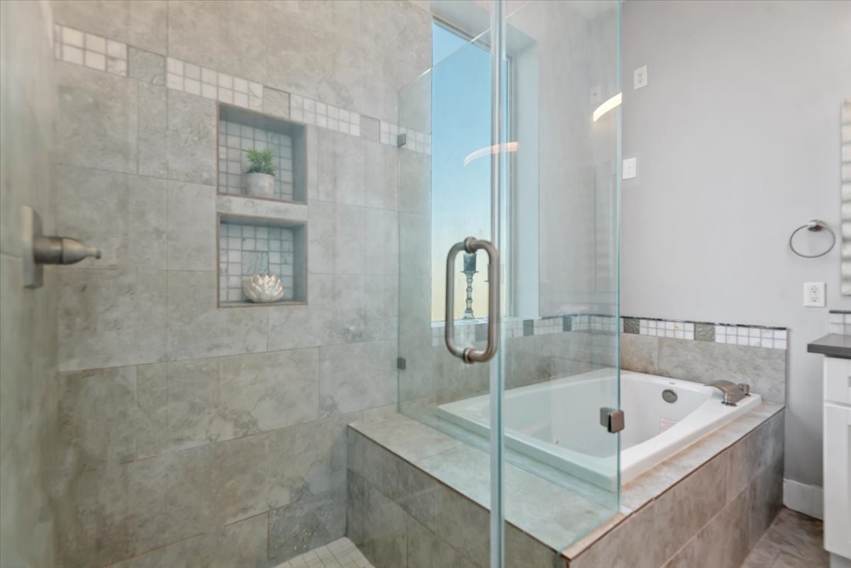 1005 Bingham Street, Unit 5 Houston, TX 77007 - Photo 38 of 50 This bathroom features a modern design with a large glass-enclosed shower and a built-in bathtub. The wall tiles have a neutral tone with decorative mosaic accents, and there are recessed shelves for added storage.