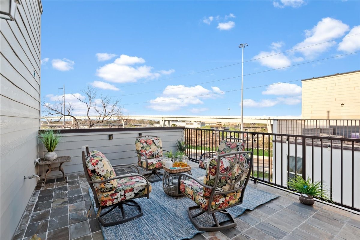 1005 Bingham Street, Unit 5 Houston, TX 77007 - Photo 42 of 50 This photo showcases a spacious outdoor patio with stylish wicker furniture and vibrant cushions. The area has slate floors and features a modern railing, offering a comfortable space for relaxation with a view of the surrounding neighborhood and clear blue skies.