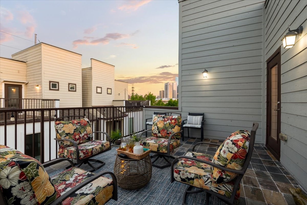 1005 Bingham Street, Unit 5 Houston, TX 77007 - Photo 43 of 50 This photo showcases a stylish rooftop patio perfect for entertaining or relaxing. The surrounding buildings and distant cityscape provide an urban backdrop, enhanced by a warm sunset glow.