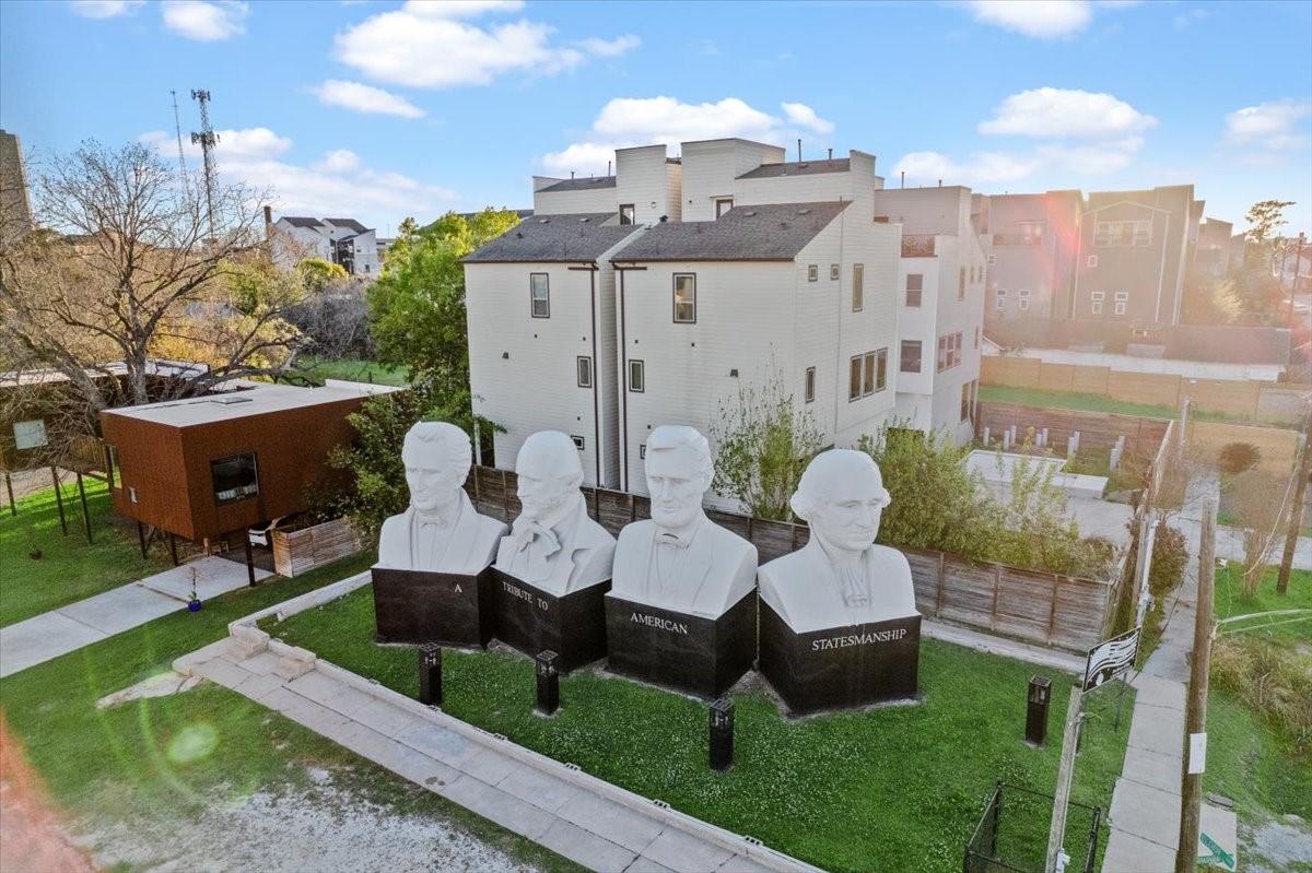 1005 Bingham Street, Unit 5 Houston, TX 77007 - Photo 45 of 50 This photo features a modern, multi-story home with a unique outdoor space showcasing large sculptures of historical figures. The property is in a well-maintained area with nearby greenery and pathways, offering a blend of art and residential living.