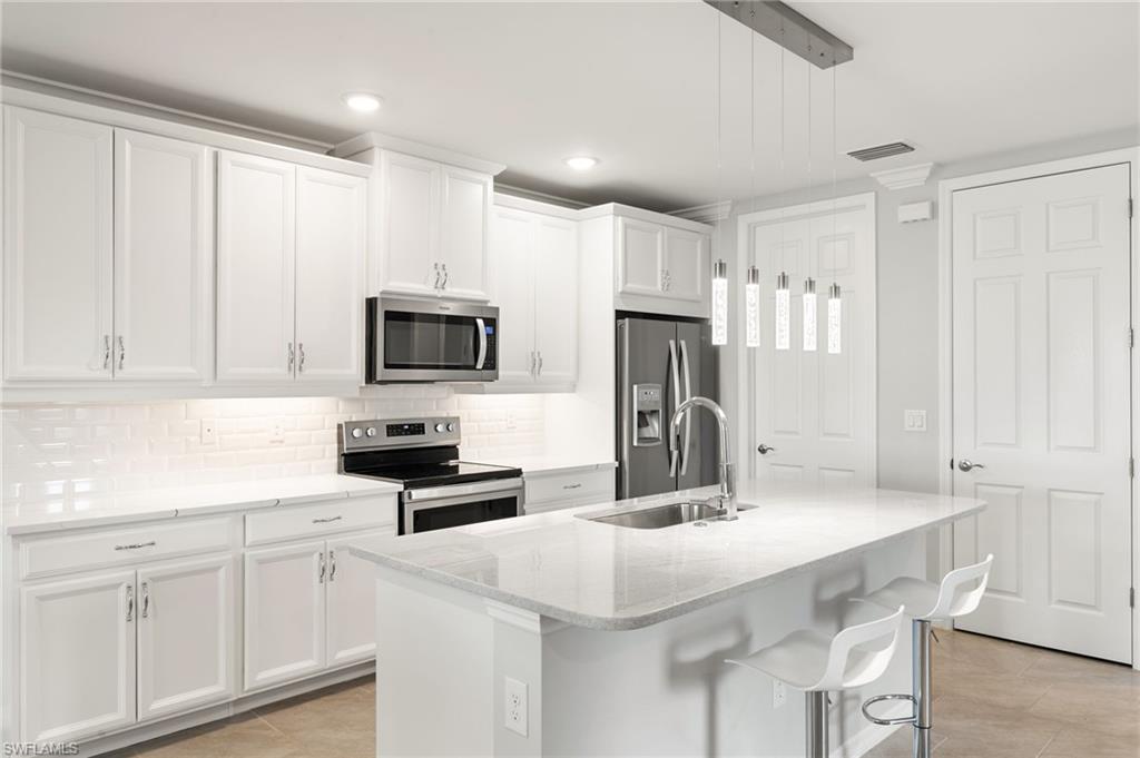 14618 Edgewater Circle Naples, FL 34114 - Photo 5 of 47 a kitchen with white cabinets and stainless steel appliances