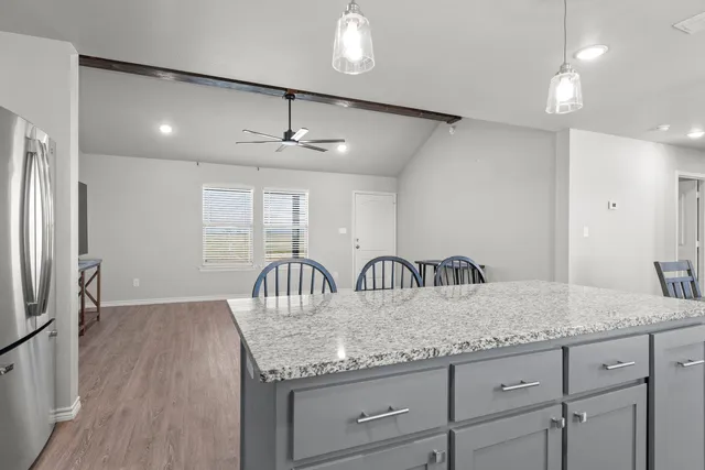 a kitchen with granite countertop stainless steel appliances a refrigerator a stove a sink a dining table and chairs with wooden floor