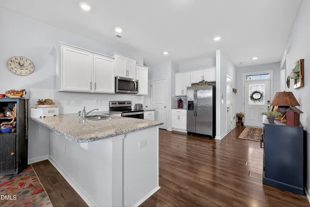 a kitchen with stainless steel appliances granite countertop a stove top oven a sink dishwasher and a refrigerator with wooden floor