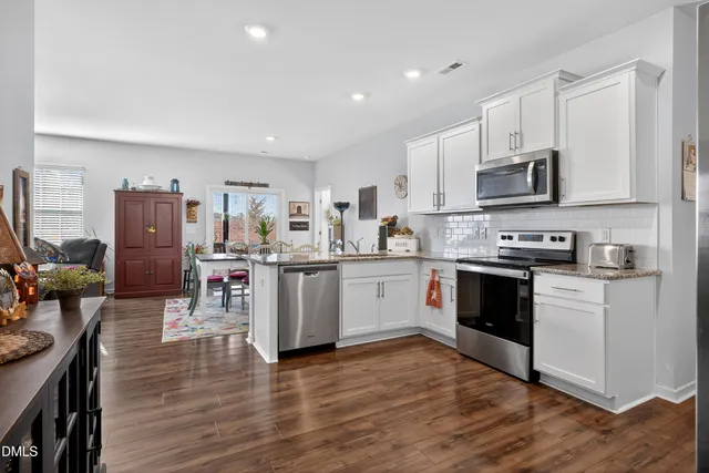 a living room with stainless steel appliances furniture wooden floor and a kitchen view