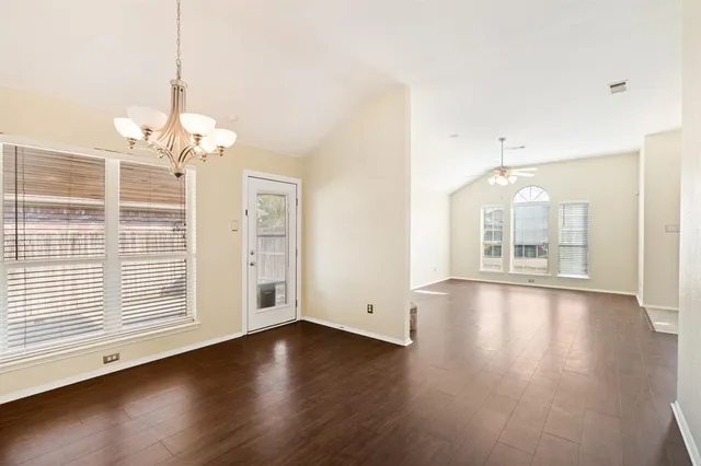 an empty room with wooden floor chandelier and windows