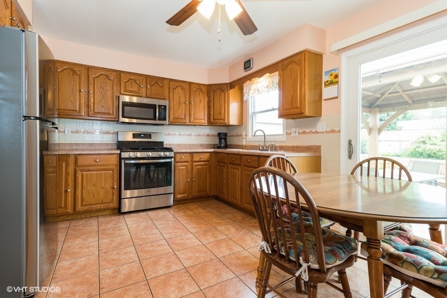 228 Murphy Drive Romeoville, IL 60446 - Photo 6 of 20 a kitchen with stainless steel appliances granite countertop a stove a sink dishwasher a dining table and chairs with wooden floor