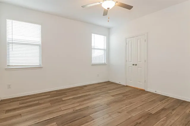 an empty room with wooden floor chandelier fan and windows