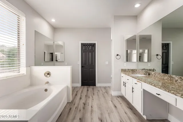 a bathroom with a granite countertop sink a mirror a bathtub and window