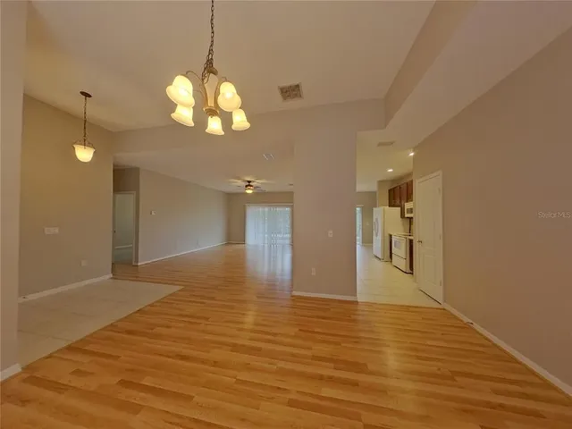 a view of an empty room and kitchen with wooden floor