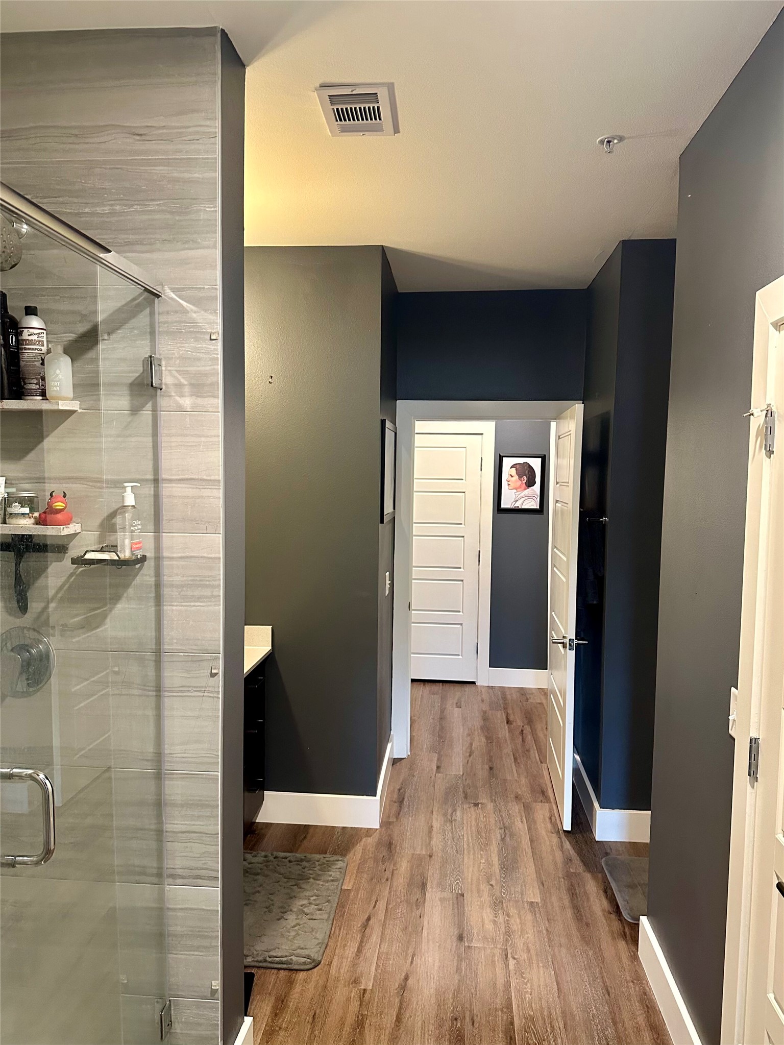 6444 Burnet Road, Unit 203 Austin, TX 78757 - Photo 16 of 30 Bathroom and hallway featuring wood-look flooring, a glass-enclosed shower with tiled walls, and a white vanity with a dark countertop